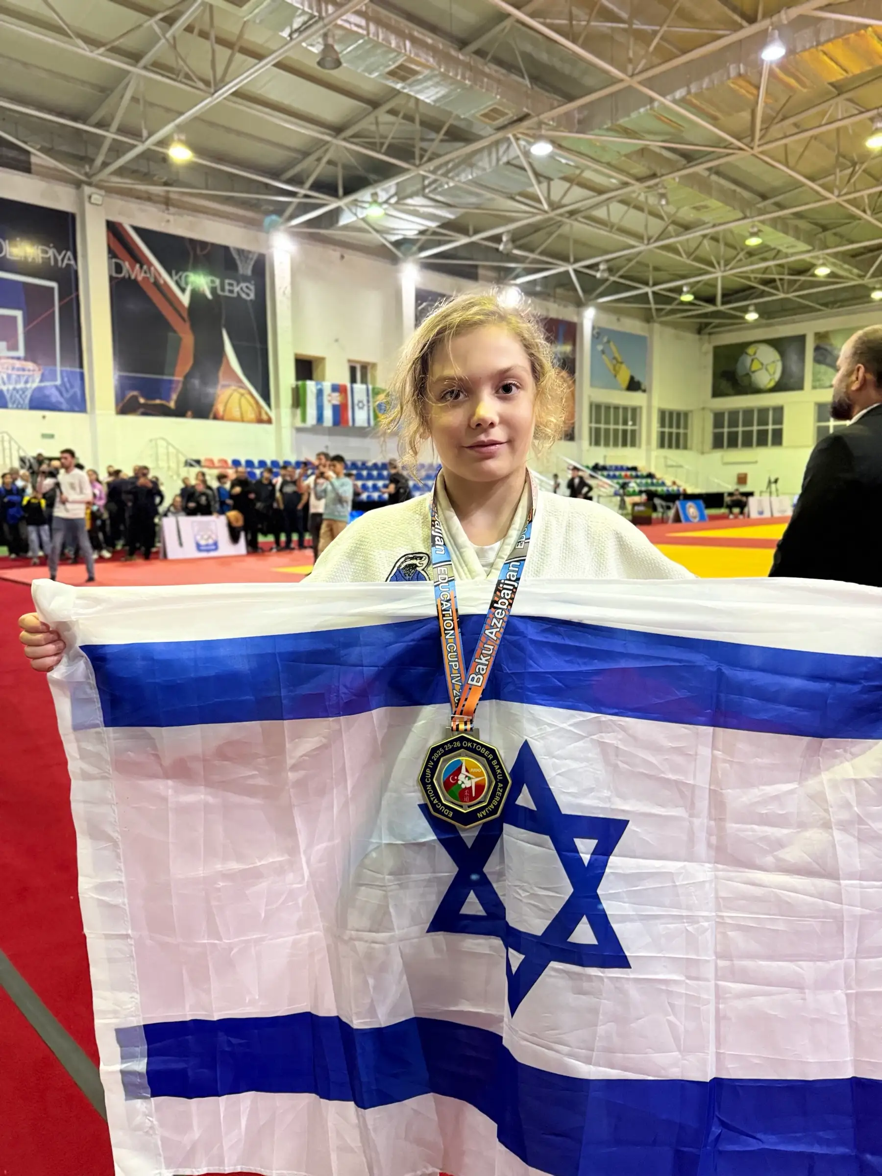 Melissa with a medal and a big Israeli flag in a sports hall