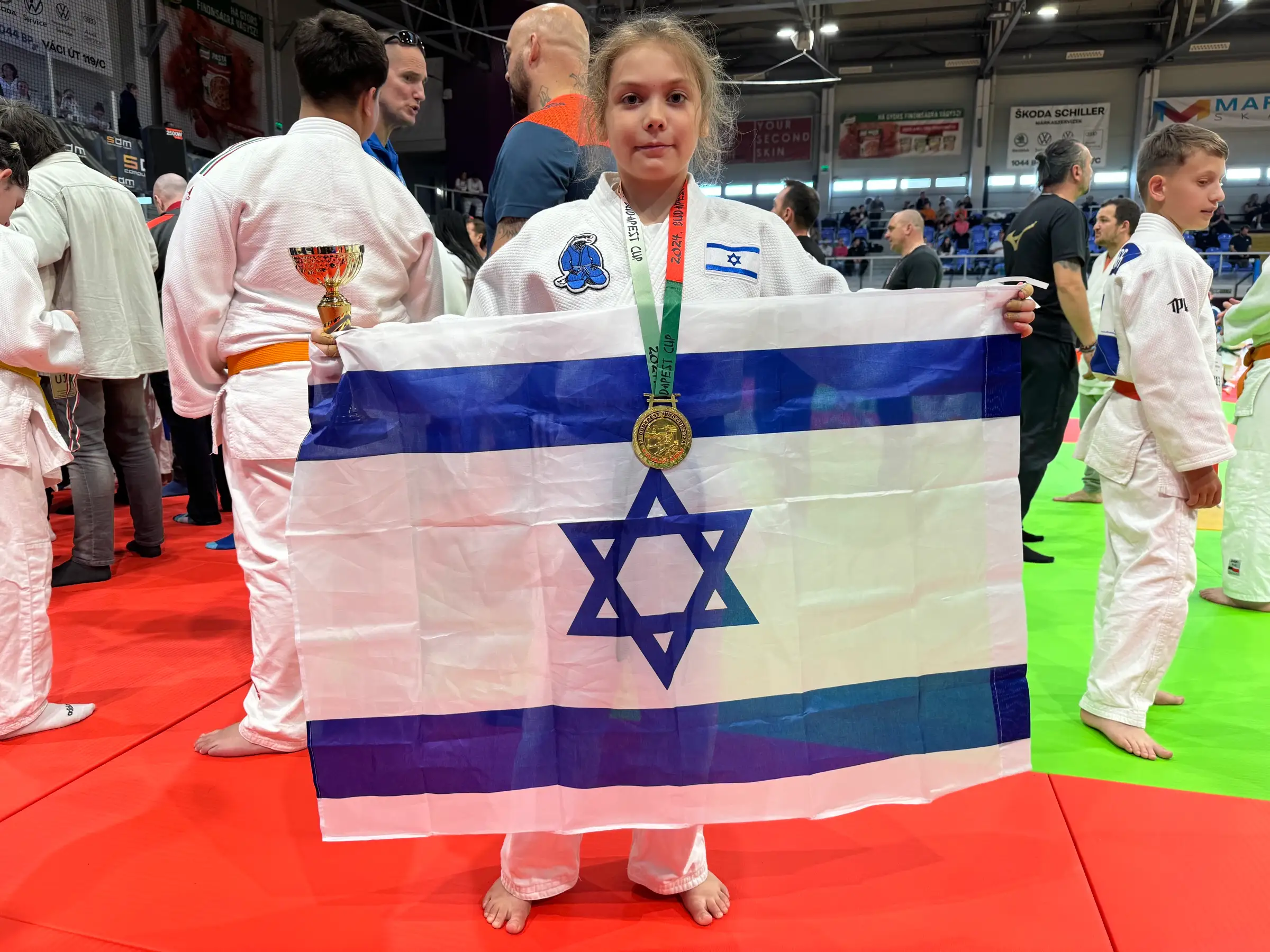 Melissa holding an Israeli flag and a medal on a competition mat