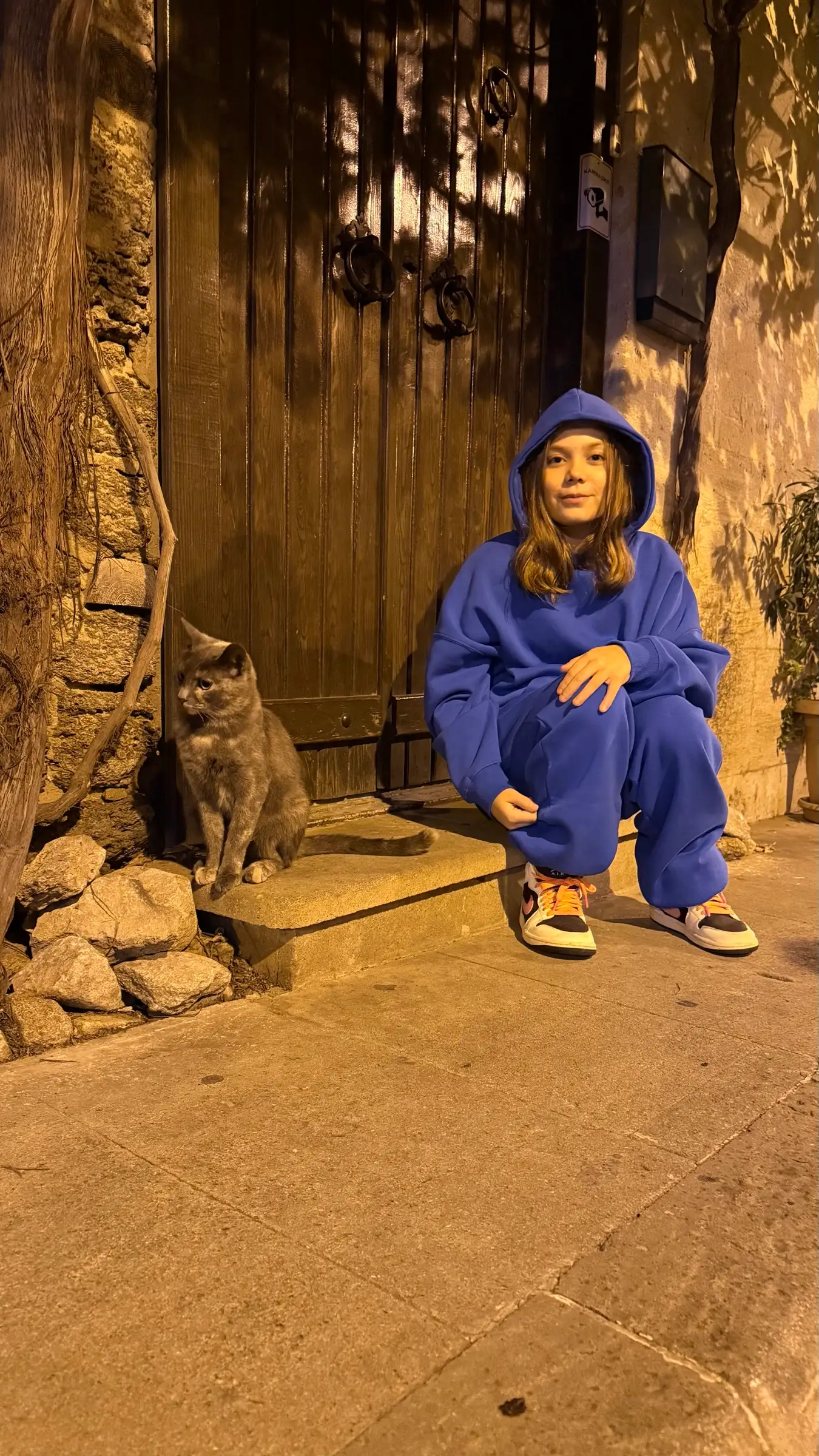Melissa in a blue tracksuit sitting next to a cat at night, in warm light
