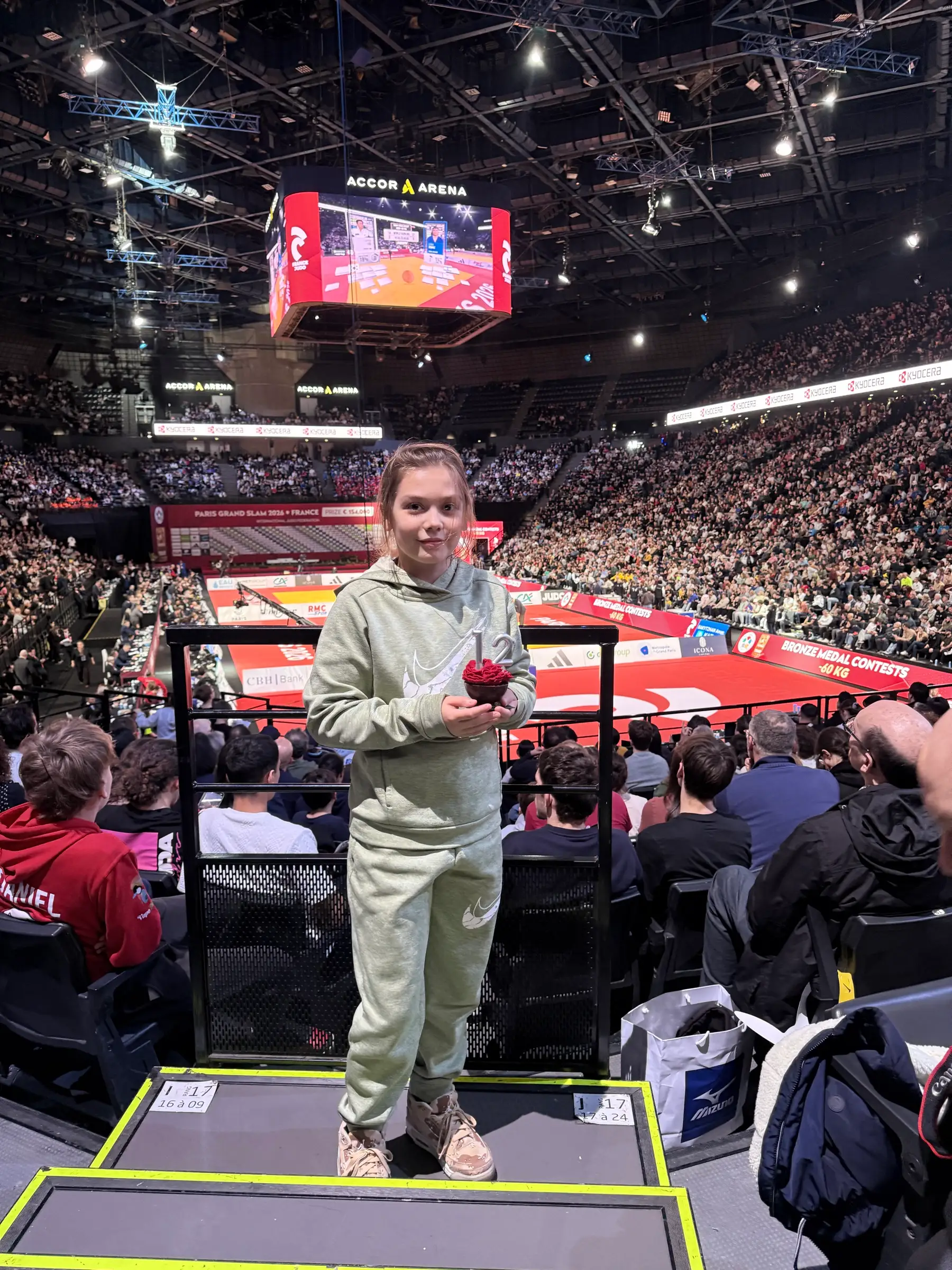 Melissa standing in front of a judo area in a large hall full of people