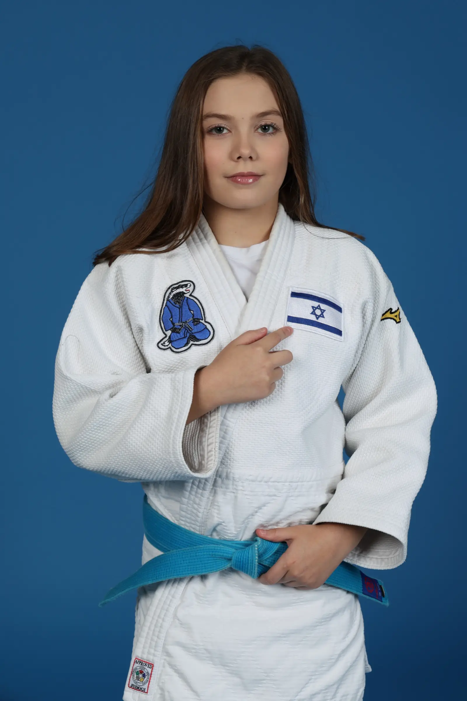 Melissa in a judo suit with the Israeli flag on her chest, hand over her heart, a studio shot