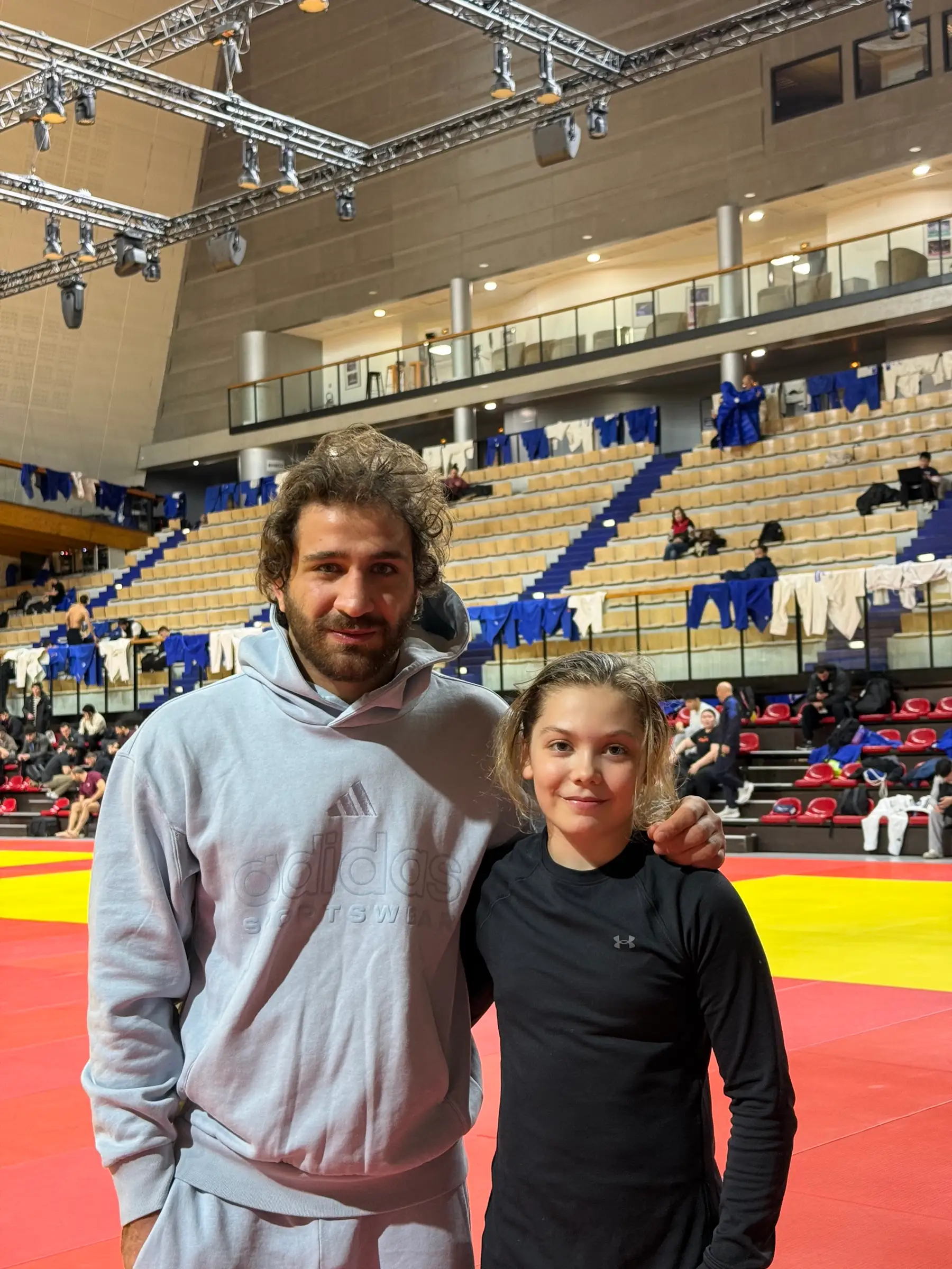 Melissa and a man in a gray sweatshirt, with the hall’s stands in the background