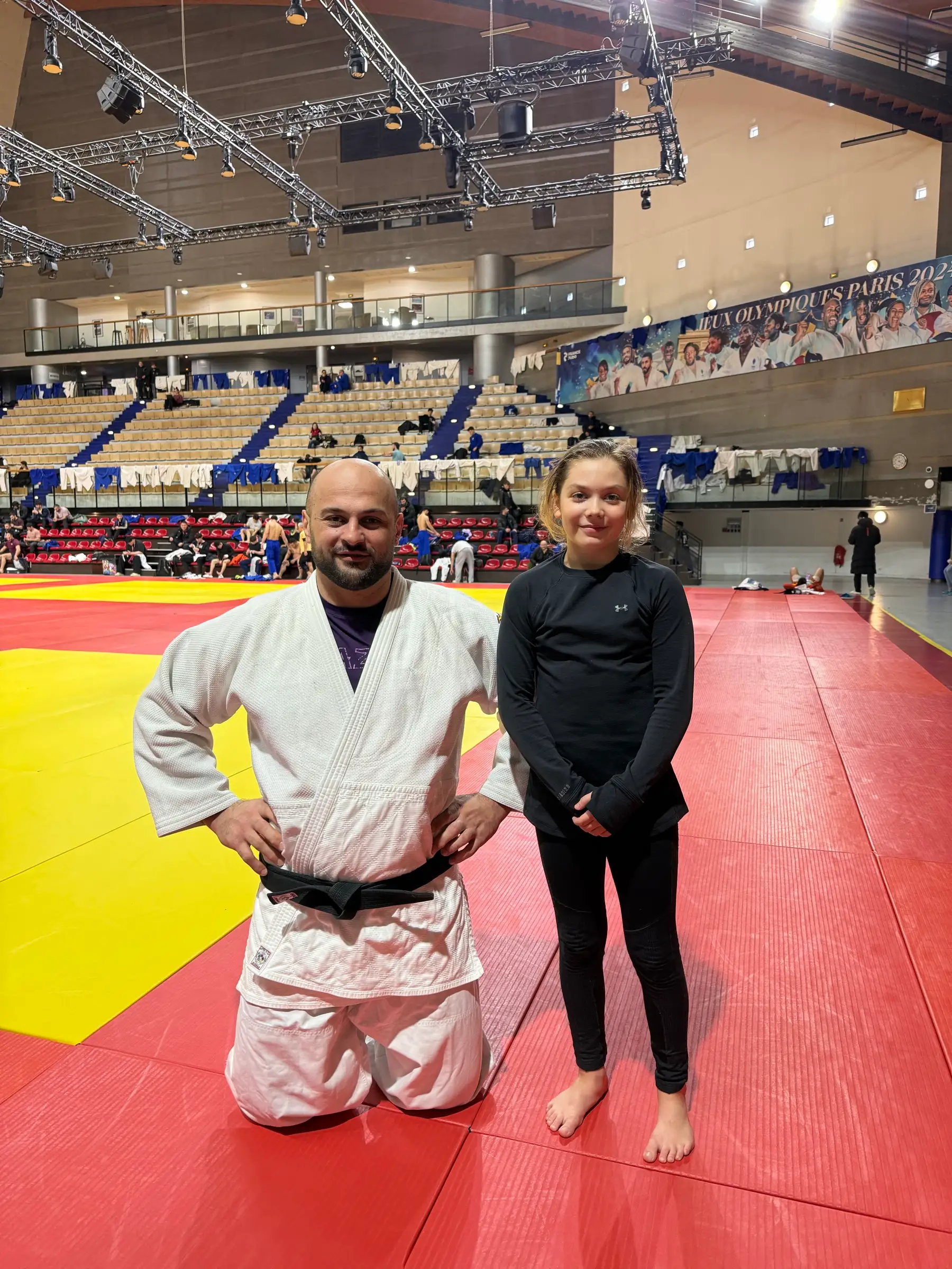 Melissa and a man in a judo suit on a red mat in a large competition hall