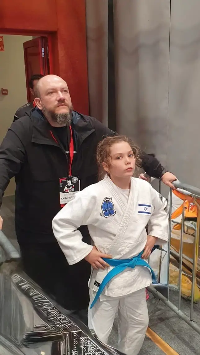 Melissa in a judo suit standing next to her father, waiting for her turn by a railing